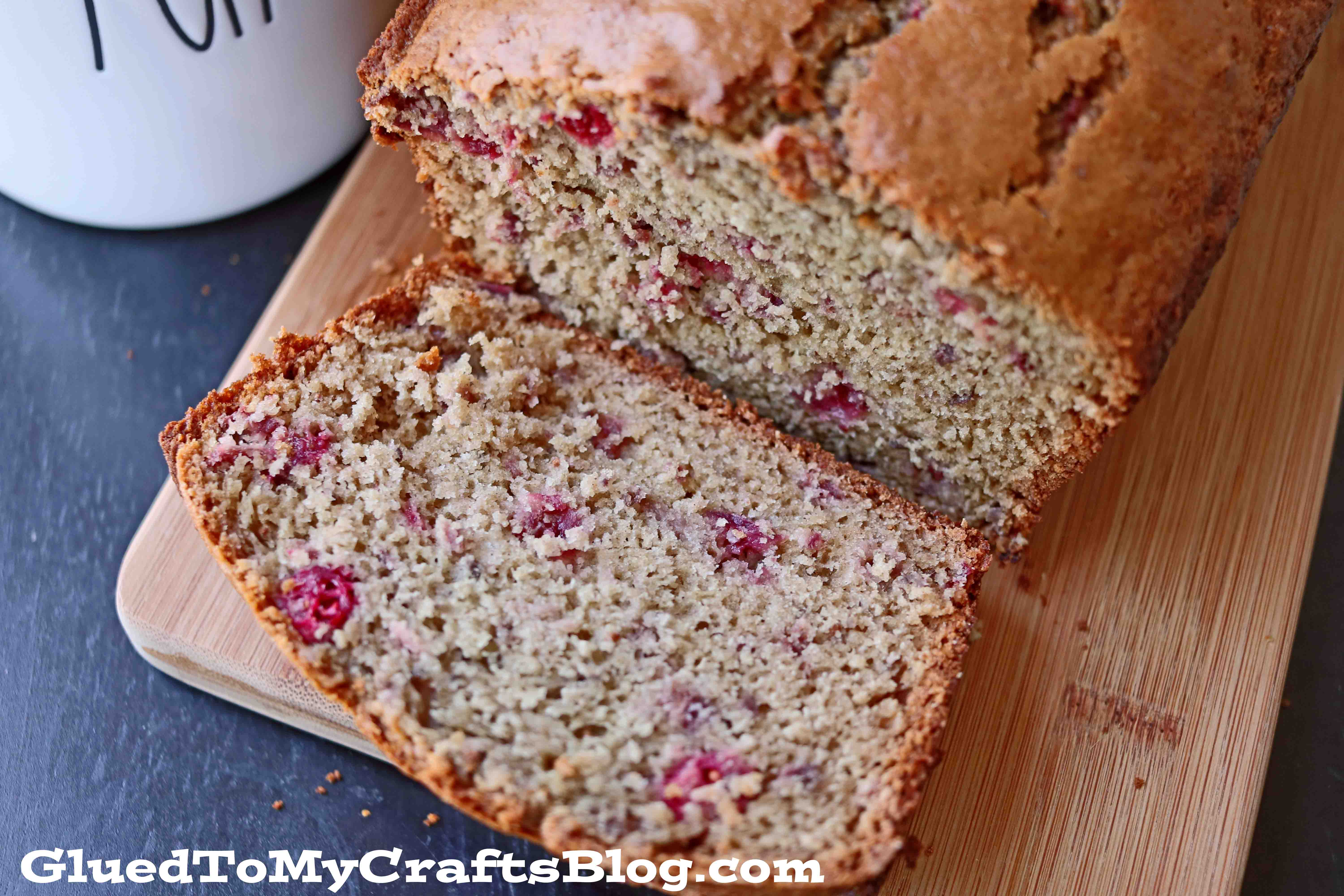 A close-up of a sliced apple cranberry bread with applesauce, featuring visible cranberries inside, rests on a wooden cutting board. The moist, dense texture stands out. The text GluedToMyCraftsBlog.com appears at the bottom of the image.