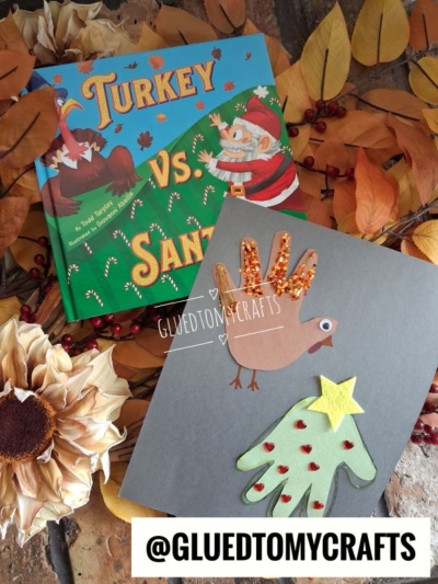 A children’s book titled Turkey vs. Santa sits next to a winter themed toddler craft featuring a brown paper handprint turkey and a green paper handprint Christmas tree.