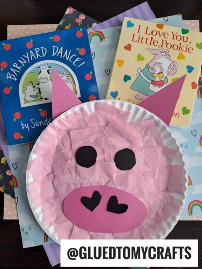 A paper plate pig with a pink tissue paper face sits atop two children's books, Barnyard Dance! and I Love You, Little Pookie. The username @GLUEDTOMYCRAFTS appears at the bottom.