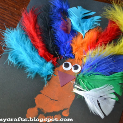 A colorful Handprint Wacky Birds turkey craft made from a brown handprint, googly eyes, a red paper wattle, a purple beak, and bright feathers in red, blue, green, yellow, black, and white on dark paper.