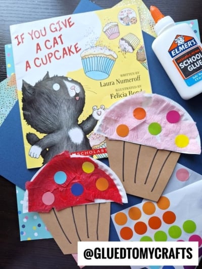 Children’s book “If You Give a Cat a Cupcake” with cat illustration, two tissue paper cupcake crafts, glue bottle, colored dot stickers, blue paper sheets, and “@GLUEDTOMYCRAFTS” watermark—perfect for cupcake kid craft fun!.