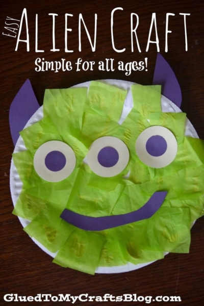 A paper plate alien craft with green tissue squares, three eyes, purple horns, and a smiling mouth sits on a dark wooden surface. Text above reads, Easy Alien Craft. Simple for all ages! This fun alien paper plate craft is perfect for creative kids and simple to make.