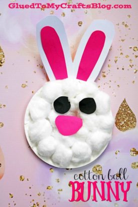 A cotton ball bunny craft featuring paper ears with pink centers and black paper eyes and nose, set on a pink and gold glittery background with text reading cotton ball BUNNY. Perfect for a fun cotton ball Easter bunny project!.