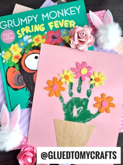 A children’s book titled Grumpy Monkey Spring Fever is next to a pink Handprint Flowerpot craft featuring green handprint stems, felt flowers, a paper pot, faux bunny ears, and more. @GLUEDTOMYCRAFTS is written at the bottom.