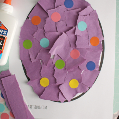A torn paper Easter egg craft features a large egg shape filled with purple paper pieces and colorful dots. A bottle of Elmer’s glue sits nearby. Text reads, “FREE PRINTABLE!!!” at the bottom.
