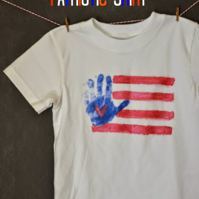 A white t-shirt hangs on a line, decorated with red stripes and a blue handprint flag, resembling an American flag. The text above reads DIY Patriotic Shirt. The bottom has the website GluedToMyCraftsBlog.com.