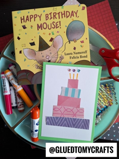 A Scrap Birthday Cards project: a cut-paper cake birthday card rests on a teal tray with markers, gems, scissors, and the book Happy Birthday, Mouse! by Laura Numeroff and Felicia Bond. @GLUEDTOMYCRAFTS text appears at the bottom.