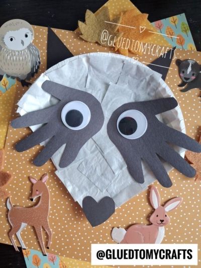Paper plate owl craft with large googly eyes and hand-shaped wings, surrounded by animal stickers such as a deer, rabbit, owl, and even a hint of a paper plate raccoon craft inspiration—all set against a playful polka-dot background. @GLUEDTOMYCRAFTS text appears on the image.