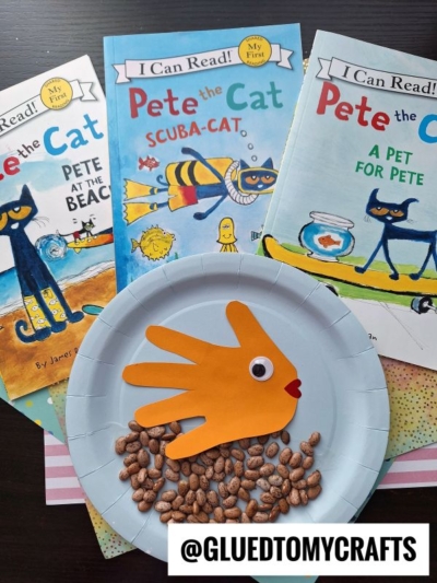 Three Pete the Cat books are displayed behind a Paper Plate Fish bowl craft with a yellow handprint fish, googly eye, and red smile. Dried beans decorate the plate as the ocean floor. @GLUEDTOMYCRAFTS is labeled in front.