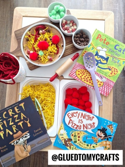 A wooden tray holds play dough, yellow yarn, red pom-poms, toy kitchen tools, and bowls of beads—perfect for Pretend Play Pizza Making—alongside three children’s books: Secret Pizza Party, Pete the Cat: Pizza Party, and Every Night is Pizza Night.