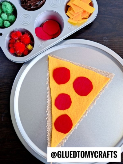 A Pretend Play Pizza Making craft features a faux pizza made of yellow and red felt on a silver tray, with a muffin tin nearby holding colored craft supplies and felt pieces. Text reads “@GLUEDTOMYCRAFTS.”.