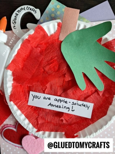 A Tissue Paper Apple craft featuring red tissue paper, a brown stem, and a green leaf. A note says "You are apple-solutely Amazing!" Surrounded by craft supplies, hearts, and @GLUEDTOMYCRAFTS text.