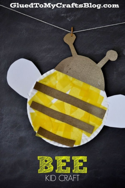 A cheerful paper plate bee craft features yellow tissue stripes, white wings, and brown antennae, hanging on a string against a black background. This adorable paper plate honey bee is a fun and simple bee craft for kids. "Bee Kid Craft" is written in yellow at the bottom.