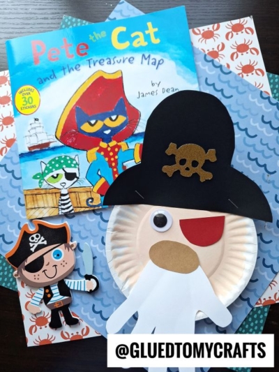 Children’s paper plate pirate crafts, including a playful paper plate pirate face, are displayed with a “Pete the Cat and the Treasure Map” book on crab-patterned paper. A watermark reads @GLUETOMYCRAFTS.