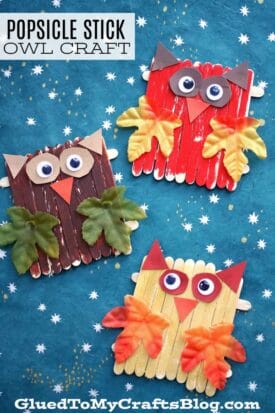 Three Popsicle Stick Owls made from craft sticks, googly eyes, paper beaks, felt wings, and faux leaves are displayed on a blue background with white stars. Text reads, Popsicle Stick Owl Craft—a charming wood owl craft for kids.