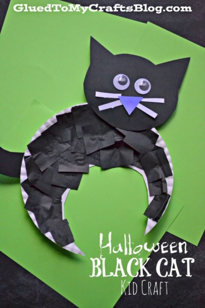A Paper Plate Black Cat craft made from black paper, googly eyes, and a paper plate on a green background. The cat features a round body, pointy ears, and a blue nose. Text reads Halloween Black Cat Kid Craft.