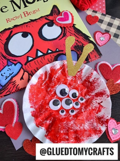 A handmade Coffee Filter Monsters red craft with googly eyes sits on heart-shaped decorations, alongside The Monster book and the handle @GLUEDTOMYCRAFTS.