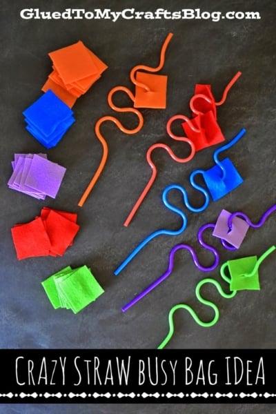 Colorful twisted straws and small squares of felt in purple, green, red, orange, and blue are arranged on a black surface, demonstrating a fun crazy straw match game craft activity for kids. Text reads: Crazy Straw Busy Bag Idea.