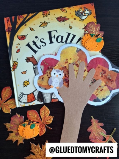 A fall-themed children’s book, felt pumpkins, and leaves surround a handprint tree craft with a paper owl and autumn leaves—perfectly capturing cozy autumn vibes. Stained Glass Fall Trees add a colorful touch to the scene. Text: @GLUEDTOMYCRAFTS at the bottom.