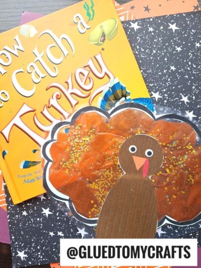A children’s book titled How to Catch a Turkey sits next to a sparkly, handmade stained glass turkey craft on star-patterned paper. The handle @GLUEDTOMYCRAFTS is displayed at the bottom.