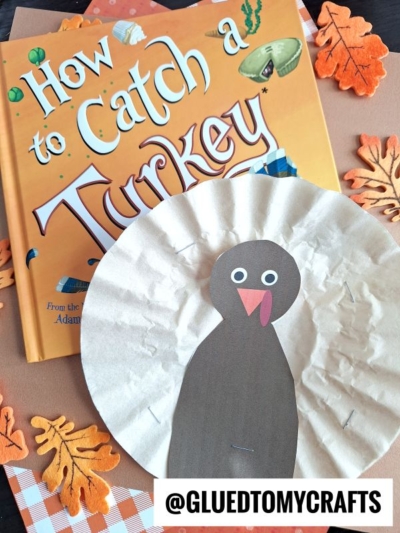 A children’s book titled How to Catch a Turkey sits next to a colorful Coffee Filter Turkeys craft, made from a coffee filter and surrounded by felt autumn leaves.