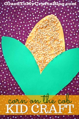 A children’s Corn On The Cob Craft project made with yellow paper, green leaf-shaped paper, and corn kernels, displayed on a purple fabric with white dots. Text reads: corn on the cob KID CRAFT.