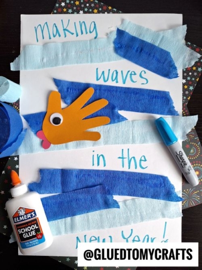 A children’s craft project with blue crepe paper strips, a hand cutout as a fish with a googly eye, and “Making waves in the New Year!”—perfect for creative new year’s keepsakes.