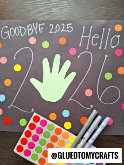 A black paper reads “Goodbye 2025, Hello 2026” with a green handprint in the center—perfect for new year's keepsakes—plus large numbers, colorful dot stickers, markers, and a @gluedtomycrafts label at the bottom.