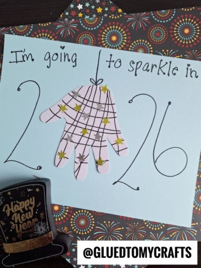 A paper handprint with star stickers and lines is placed as the 0 in 2026 on blue paper with the text "I'm going to sparkle in 2026," surrounded by fireworks-themed paper and a Happy New Year decoration—perfect for new year's keepsakes.