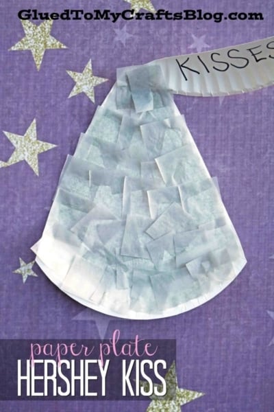 A Paper Plate Hershey Kiss craft, made with silver tissue squares and a “KISSES” tag on top, sits on a purple background sprinkled with gold stars—perfect for anyone who loves making a paper plate chocolate kiss.