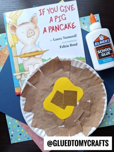 A children’s book titled “If You Give a Pig a Pancake,” Elmer’s school glue, colorful craft paper, and a fun Paper Plate Pancake craft with two yellow squares on top. Text: @GLUEDTOMYCRAFTS.