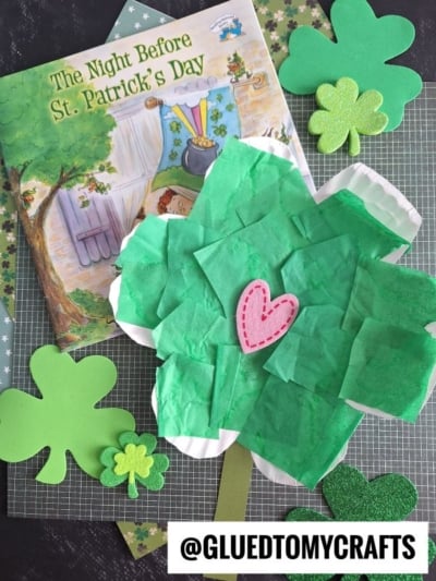 A children’s book titled “The Night Before St. Patrick’s Day” is next to shamrock crafts, including a Paper Plate Clover with a pink heart and smaller green shamrock cutouts. @GLUEDTOMYCRAFTS is written below.
