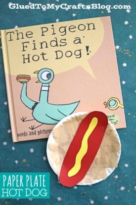 A children’s book titled The Pigeon Finds a Hot Dog! is shown next to a colorful hot dog paper plate craft made with red and yellow paper. The teal background features scattered star designs for a playful touch.