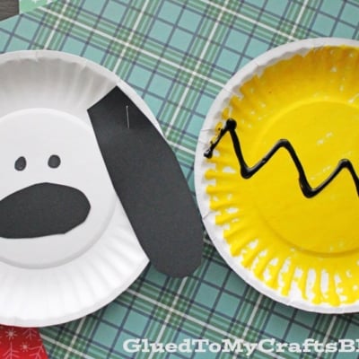 Two paper plate crafts: one is a paper plate Snoopy kid craft with black ears and nose, and the other is a yellow plate with a black zigzag line like a Charlie Brown kid craft, both on a plaid background.