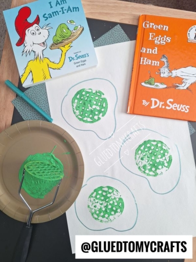 A fun Dr Seuss Kid Crafts project inspired by Green Eggs and Ham, featuring green paint egg stamps made with a potato masher and two Dr. Seuss books in the background.