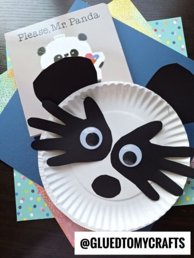A paper plate panda craft featuring black paper cutouts for ears and eyes, displayed on colorful sheets next to the children’s book Please, Mr. Panda. This adorable paper panda craft makes storytime even more fun!.