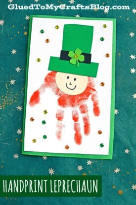A handmade leprechaun handprint card features a cheerful leprechaun with a green hat atop a red handprint, embellished with sequins on a green background. Text reads Handprint Leprechaun.