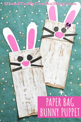 Two paper bag bunny puppets with white and pink paper ears, black whiskers, and button noses are displayed on a teal background with small white stars. Perfect as an Easter bunny paper bag craft for kids! Text reads “Paper Bag Bunny Puppet.”.