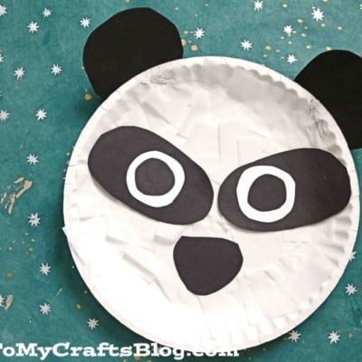 A cute paper panda craft made from a white paper plate and black and white cutouts for the eyes, nose, ears, and mouth, displayed on a teal background with white star pattern