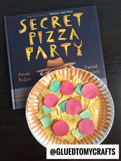 A paper plate pepperoni pizza craft with red, pink, and green paper toppings sits in front of the book Secret Pizza Party by Adam Rubin and Daniel Salmieri on a dark table. The Instagram handle @GLUEDTOMYCRAFTS is visible.