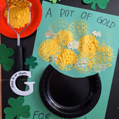 A St. Patty’s Day craft features a paper pot with yellow stamped paint gold coins, surrounded by green shamrocks and the text “A pot of gold for you!” The handle @GLUEDTOMYCRAFTS is visible at the bottom.