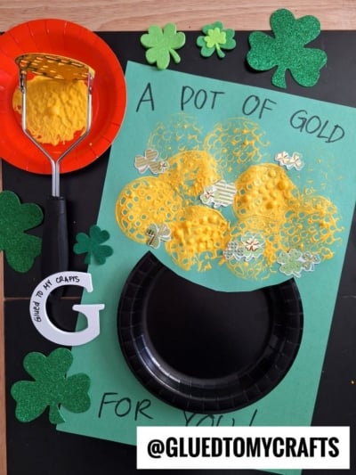 A St. Patty’s Day craft features a paper pot with yellow stamped paint gold coins, surrounded by green shamrocks and the text “A pot of gold for you!” The handle @GLUEDTOMYCRAFTS is visible at the bottom.