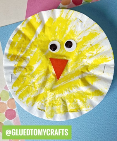 A charming Easter Kid Craft, this paper plate chick painted yellow with googly eyes and an orange paper beak sits on blue polka dot paper. The text @GLUEDTOMYCRAFTS appears at the bottom.