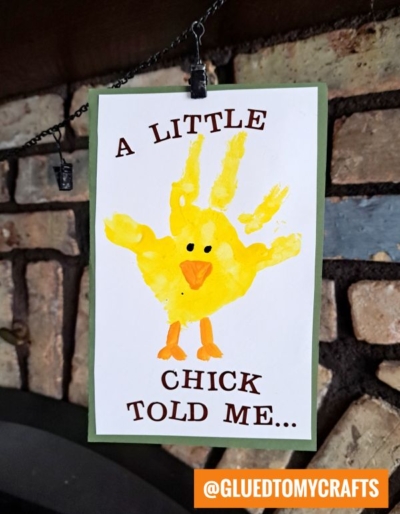 A handmade card with a yellow chick crafted from a child’s handprint, googly eyes, orange beak and feet, and the words “A LITTLE CHICK TOLD ME…”—a sweet addition to your collection of handprint gift ideas.