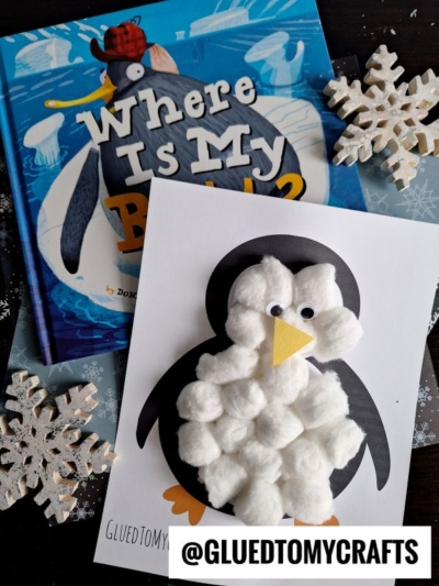 A children’s book titled Where Is My Butt? lies next to a cotton ball penguin craft on paper. Decorative snowflakes are scattered around. The username @GLUEDTOMYCRAFTS is at the bottom.