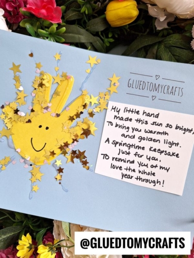 A handmade Easter Kid Craft card with a yellow handprint sun, surrounded by star-shaped confetti. A handwritten note reads: My little hand made this sun so bright to bring you warmth and golden light... Flowers are in the background.