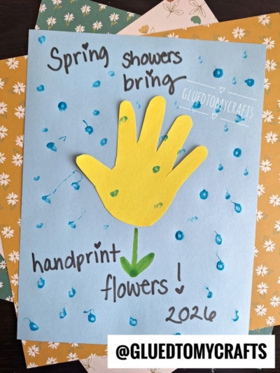 A blue card decorated with blue dots and the text "Spring showers bring handprint flowers! 2026." An Easter Kid Craft, it features a yellow paper handprint as the flower, highlighted by a green arrow, with patterned paper in the background.