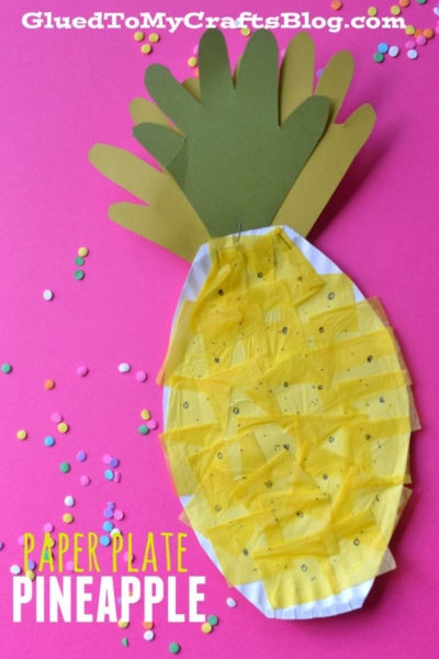 A vibrant paper plate pineapple craft made by covering a paper plate with yellow tissue paper and adding green paper leaves, displayed on a pink background scattered with colorful confetti. Text reads “Paper Plate Pineapple.” This cheerful tissue paper pineapple is perfect for summer crafting fun!.