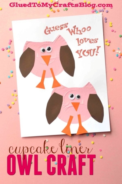 A cupcake liner owl card featuring two pink owls with orange feet and beaks, brown wings, and googly eyes sits on a sprinkle-decorated pink background. Text reads: Guess Whoo loves YOU! This cupcake liner owl craft is sweet and fun to make.