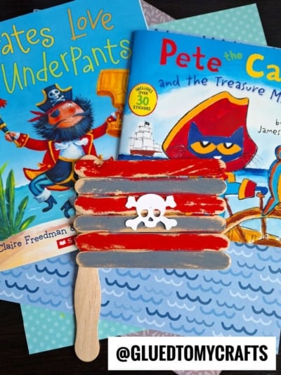 Two childrens books, Pirates Love Underpants and Pete the Cat and the Treasure Map, are shown alongside popsicle stick pirate flags crafted from colored sticks, featuring a white skull and crossbones.